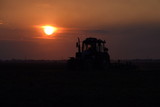 Tractor plowing plow the field on a background sunset. tractor silhouette on sunset background