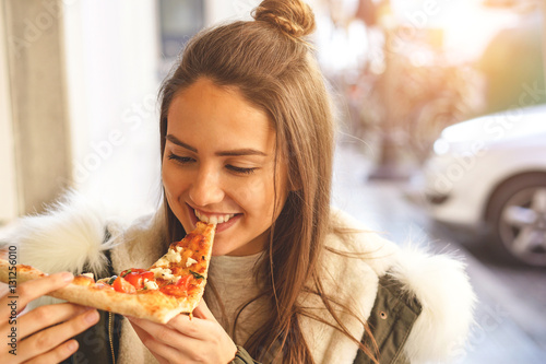 Beautiful young girl eating a slice of pizza in the street - Portrait of a pretty girl eating outside