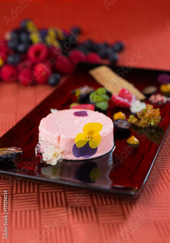 A beautiful rich gourmet blueberry and raspberry cheesecake  garnished with rose petals on a modes black plate.