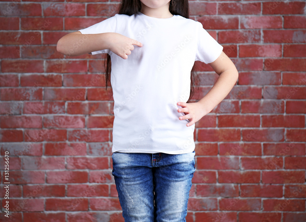 Little girl in blank white t-shirt standing against brick wall, close up Little girl in blank white t-shirt standing against brick wall, close up