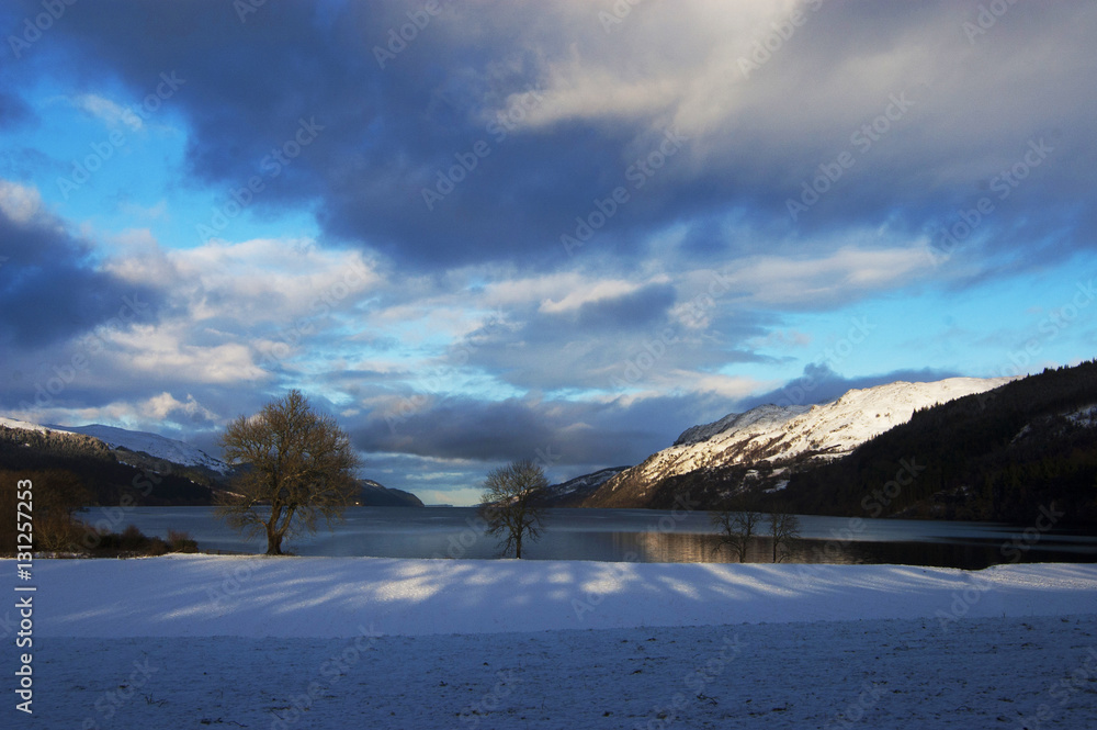 Winter evening on Loch Ness lake with trees and dramatic sky