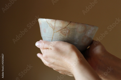 金継されたピンクの日本の抹茶茶碗を両手で持つぼかした背景