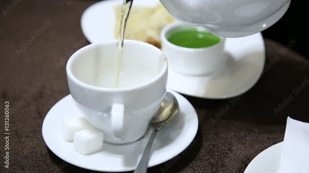 Pouring tea into white cup on table from porcelain kettle. jelly and pancake on a background Pouring tea into white cup on table from porcelain kettle. jelly and pancake on a background
