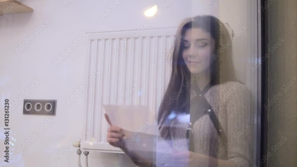 Portrait of stylish young woman with brown hairs reading letter and smiling by the window. Portrait of stylish young woman with brown hairs reading letter and smiling by the window.