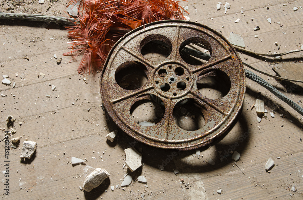 Fototapeta premium An old metal rusty cinematography cinema film reel, that has been left in an abandoned cinema amongst concrete debris.