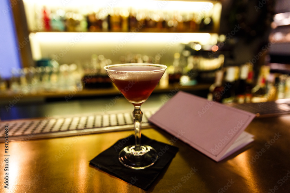 A dark image of a cocktail in a martini glass on a bar stand, menu, bokeh, small depth of field. A dark image of a cocktail in a martini glass on a bar stand, menu, bokeh, small depth of field.