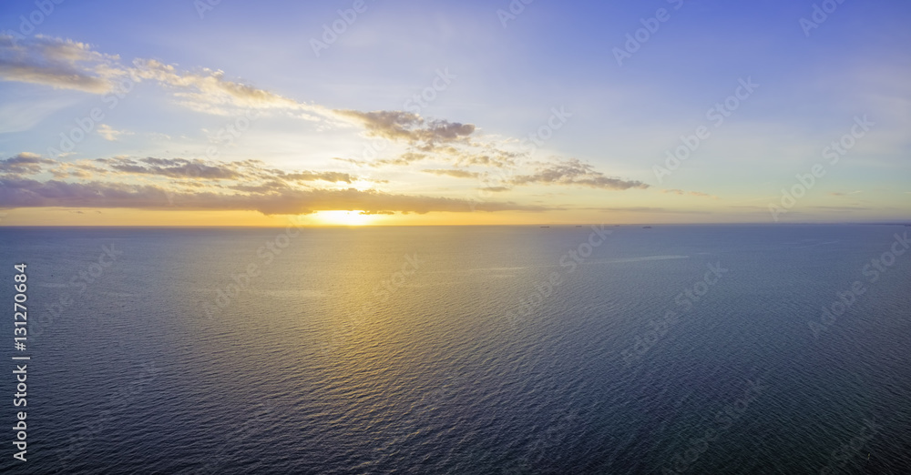Beautiful glowing yellow-purple sunset over ocean waters with tiny ships in the distance