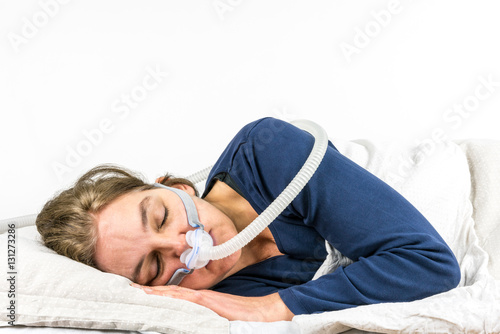 Woman sleeping  on her side with CPAP, sleep apnea treatment. Studio portrait white background.