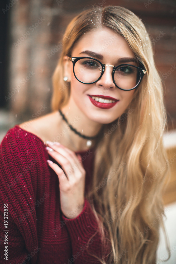Blonde girl with glasses, smiling in a burgundy sweater, snow, winter Blonde girl with glasses, smiling in a burgundy sweater, snow, winter