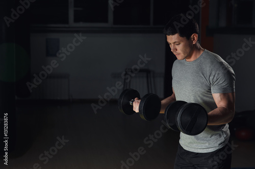 very power athletic guy bodybuilder, execute exercise with dumbbells, in dark gym.