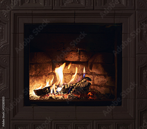 Cozy vintage fireplace with white tiles with flames of fire in it