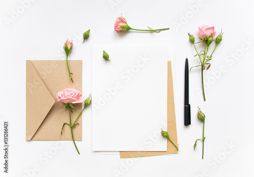 Letter and eco paper envelope on white background. Invitation cards, or love letter with pink roses. Holiday concept, top view, flat lay