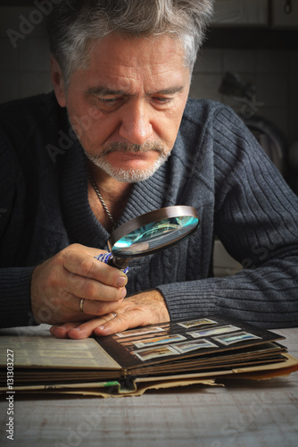 Man considers album of stamps trough the magnifying glass