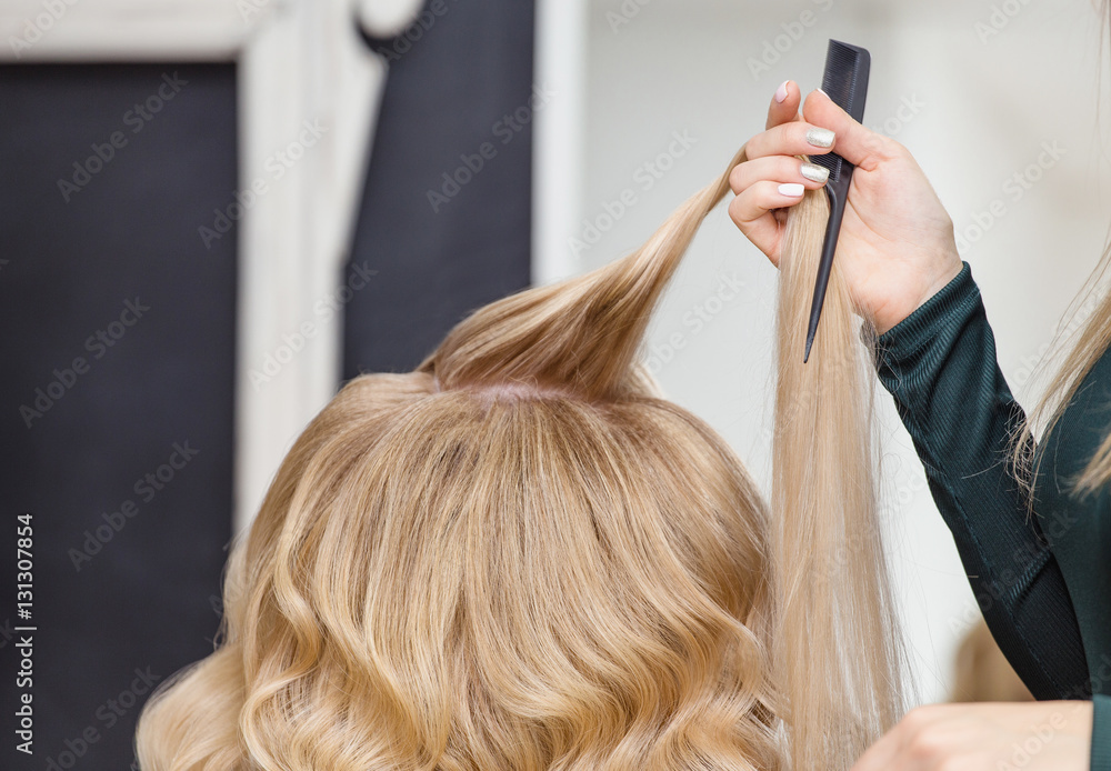 Fototapeta premium Back View Of A Beautiful Blond Woman With Long Hair and hairdresser hand with hairbrush.