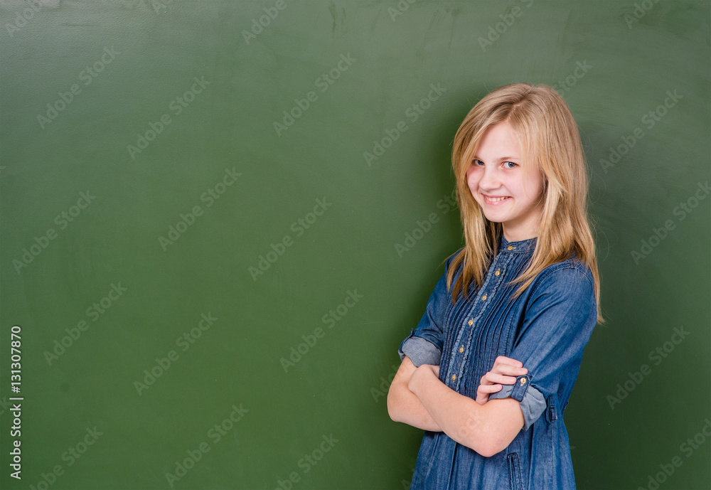 Young girl standing near empty green chalkboard. Space for text Young girl standing near empty green chalkboard. Space for text