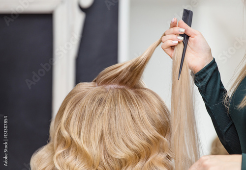 Back View Of A Beautiful Blond Woman With Long Hair and hairdresser hand with hairbrush.
