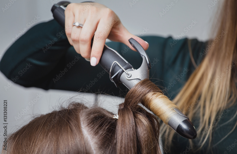 Fototapeta premium stylist making ringlets to brunette woman. Hairdresser working with beautiful woman hair in hairdressing salon