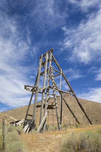 Old mining head frame in the Nevada Desert under blue sky with clouds.