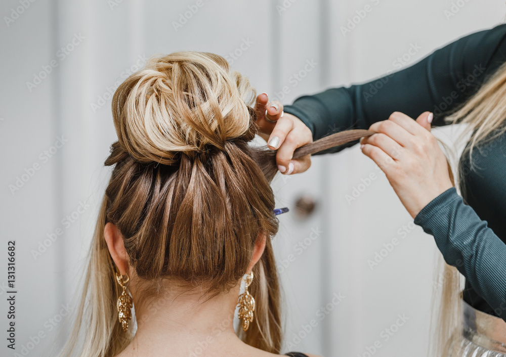 Fototapeta premium Hairdresser makes complex and beautiful hairstyle upper bun. Suitable for evening and wedding style