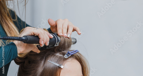 stylist making ringlets to brunette woman. Hairdresser working w
