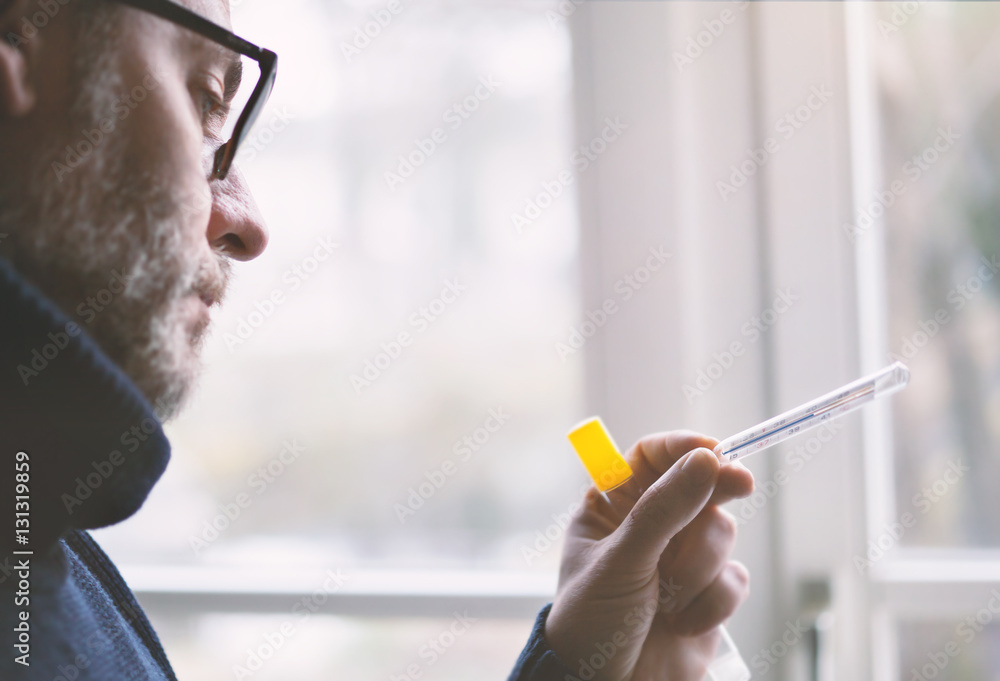 Mann mit Erkältung schaut auf fieberthermometer Mann mit Erkältung schaut auf fieberthermometer
