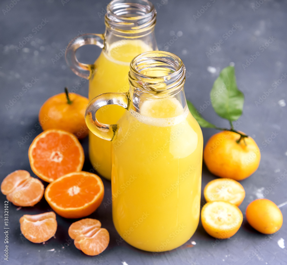 Two bottles of citrus juice served with fresh whole and slice citrus on gray background Two bottles of citrus juice served with fresh whole and slice citrus on gray background