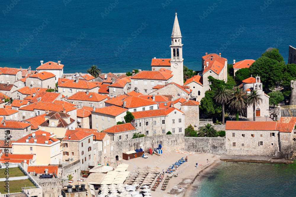 Fototapeta premium Bell tower of the Old Town of Budva city and Ricardova Glava beach. Aerial view with houses roofs. Adriatic sea. Montenegro