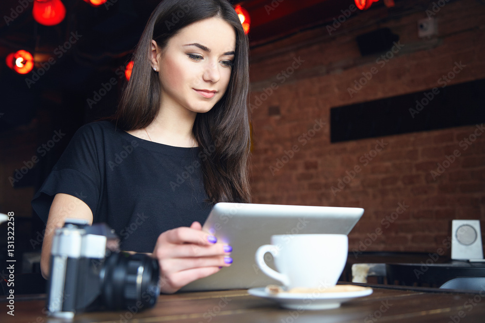 Young female attractive student with long straight hair working on tablet while sitting alone in coffee shop during free time. Lifestyle, leisure time Young female attractive student with long straight hair working on tablet while sitting alone in coffee shop during free time. Lifestyle, leisure time