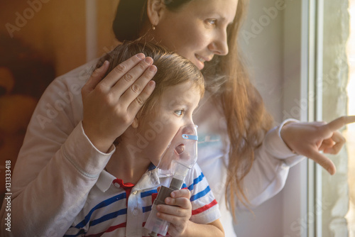 Young woman with son doing inhalation with a nebulizer at home