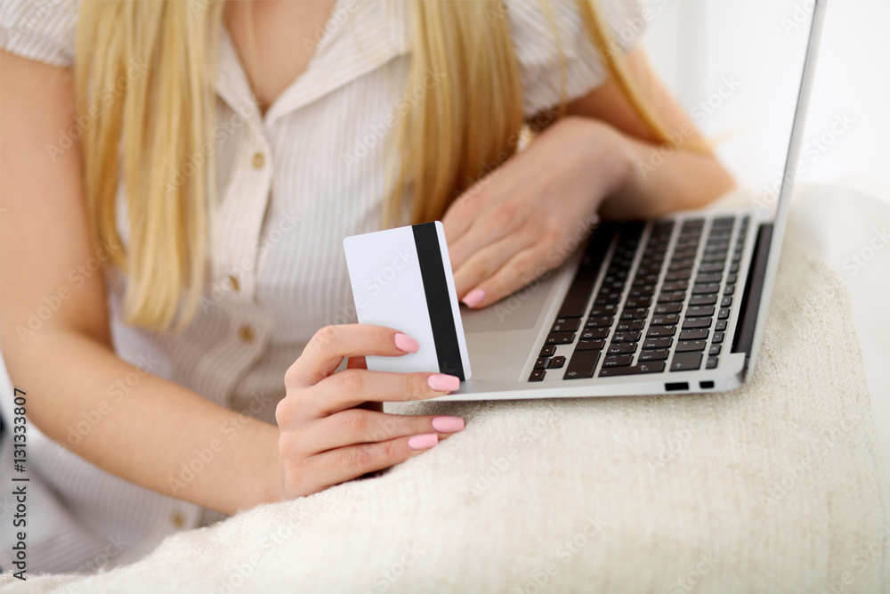 Happy woman doing online shopping at home . Close- up of a hand holding a credit card next to a laptop Happy woman doing online shopping at home . Close- up of a hand holding a credit card next to a laptop