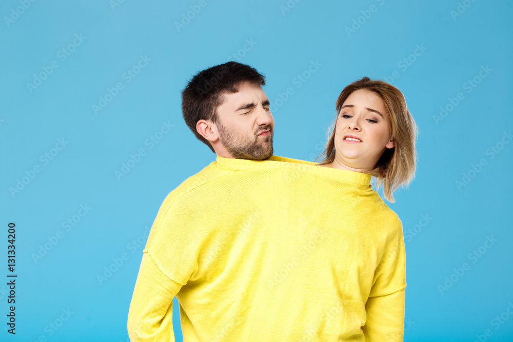 Fototapeta premium Displeased young couple in yellow sweater posing over blue background.