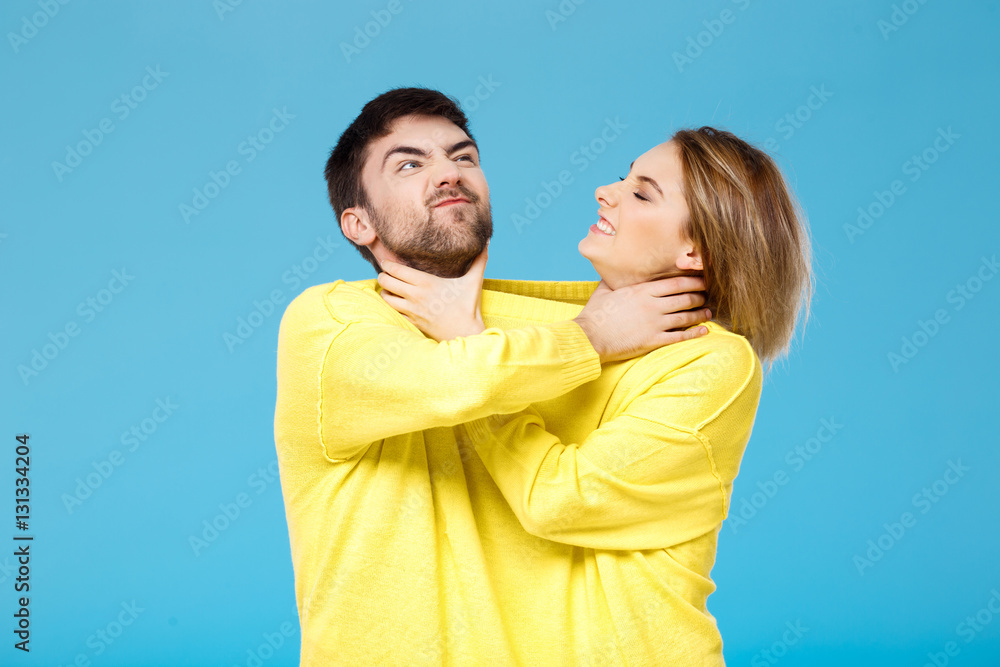 Fototapeta premium Young beautiful couple smohering each other over blue background.