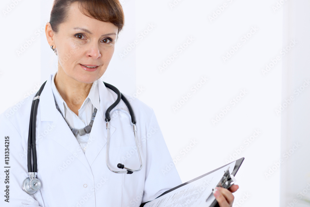 Happy female doctor standing in hospital and filling up medical form. Medicine and health care concept. Happy female doctor standing in hospital and filling up medical form. Medicine and health care concept.