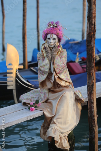 Venice Carnival - young lady with golden and pink mask on the pier with gondolas
