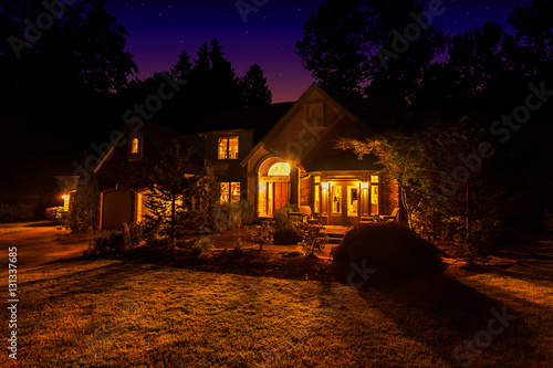 Foto Suburban home at night with windows lit up and light spilling out onto the front