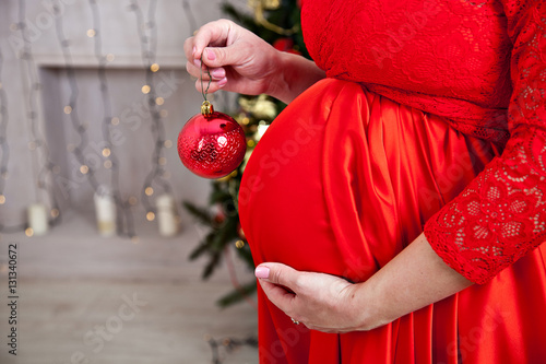 belly of a pregnant woman in a red dress with a New Year's ball