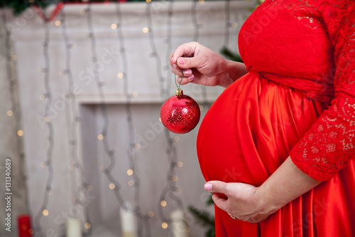belly of a pregnant woman in a red dress with a New Year's ball