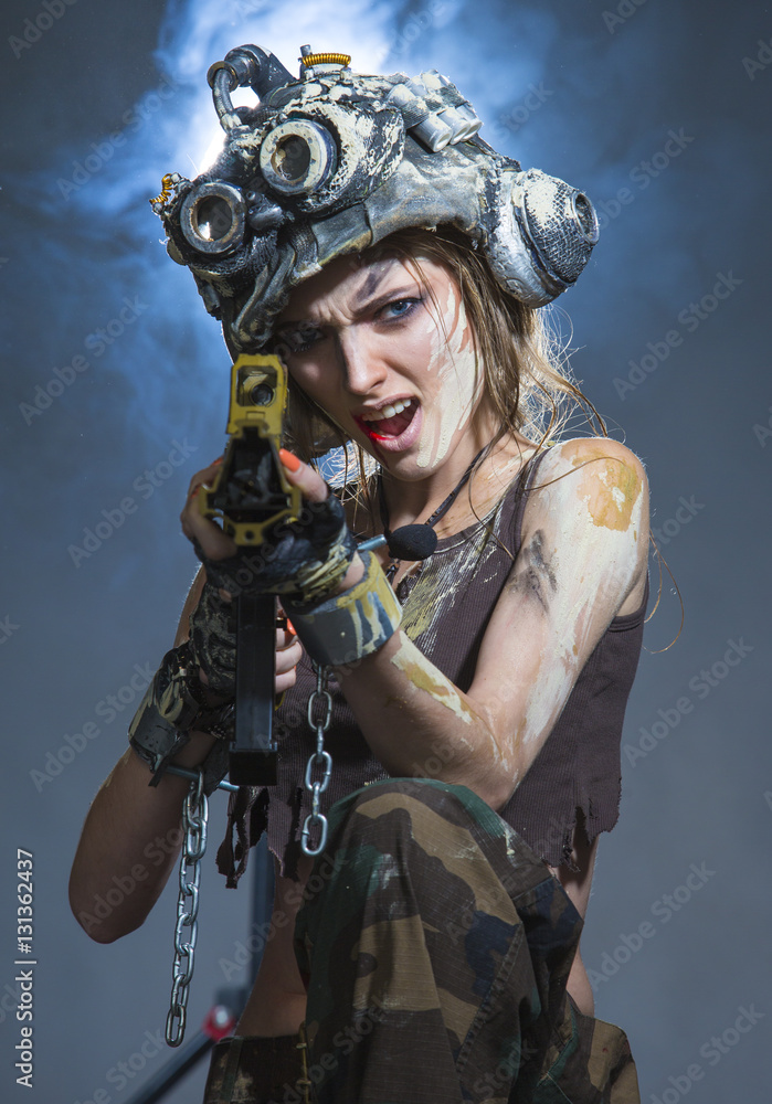 Obraz premium Young woman - soldier in a helmet, is shooting a machine gun