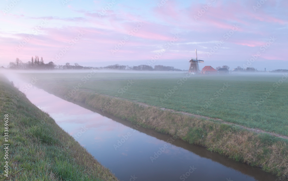 Dutch windmill by river in mist