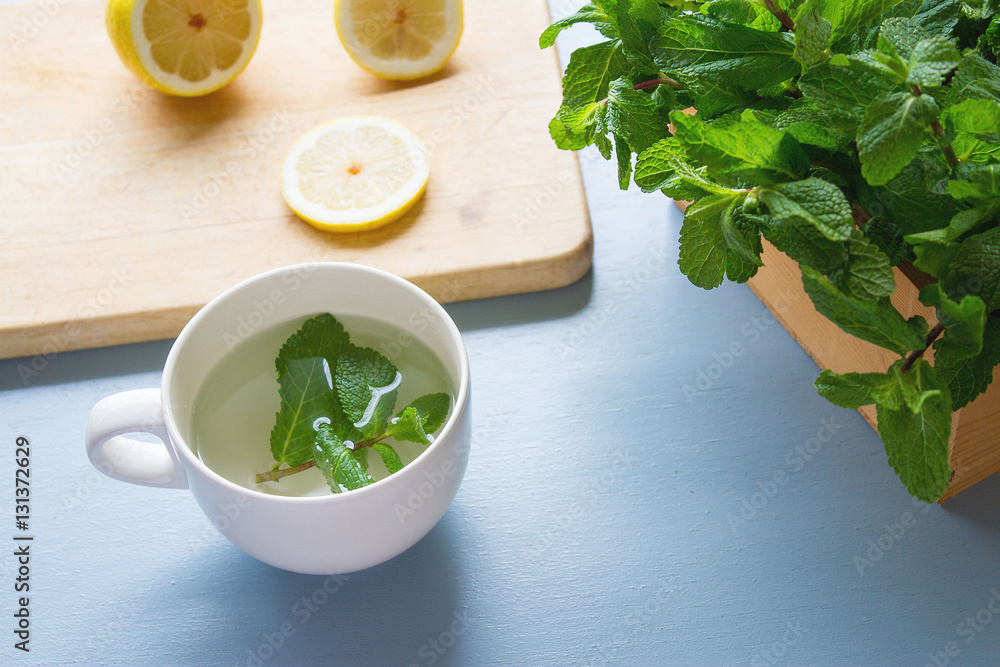 An ingredients for peppermint tea on light blue rustic table, lemon slices on chopping board,fresh mints in wooden box with peppermint leaves laying on table, healthy drink for winter,release stress An ingredients for peppermint tea on light blue rustic table, lemon slices on chopping board,fresh mints in wooden box with peppermint leaves laying on table, healthy drink for winter,release stress
