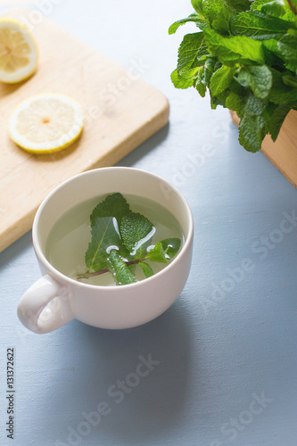 An ingredients for peppermint tea on light blue rustic table, lemon slices on chopping board,fresh mints in wooden box with peppermint leaves laying on table, healthy drink for winter,release stress