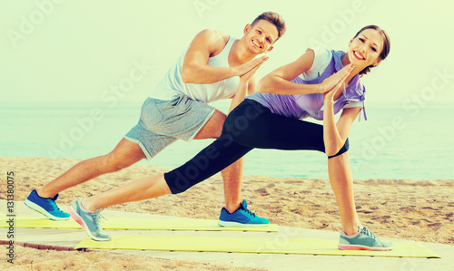 Guy and girl practising yoga poses standing on beach