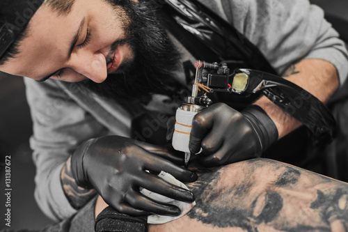 Tattoo master in black gloves  tattoo on the skin of black ink tattoo of his client in the salon.