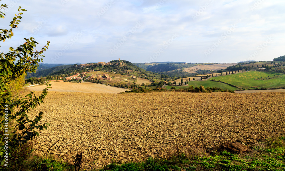 Obraz premium Rural landscape in Italy, Tuscany, hills, road winds up the mountain, on the mountain city Montechello, arable land and cypresses.