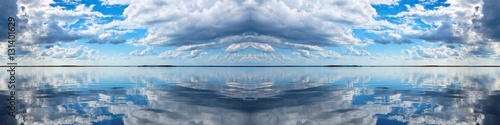 Cloudscape Panorama. Spectacular blue and white panoramic cloudscape with clear water reflections. Photograph was shot at sea from the deck of a boat looking toward land. 