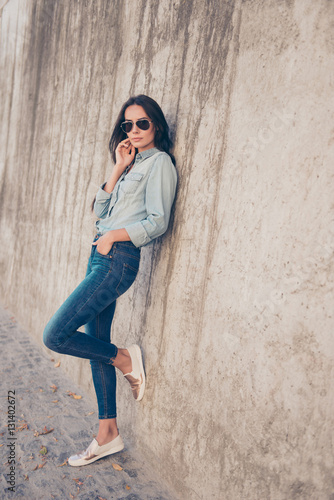 Young woman in glasses wearing jeans clothes standing near ston