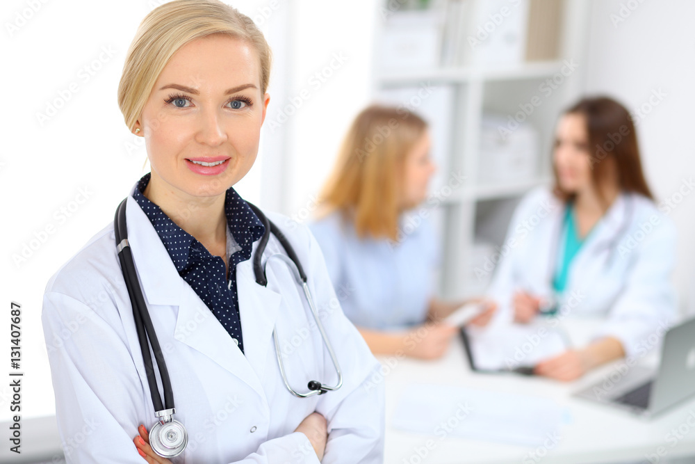 Female doctor smiling on the background with patient and his physician in hospital Female doctor smiling on the background with patient and his physician in hospital