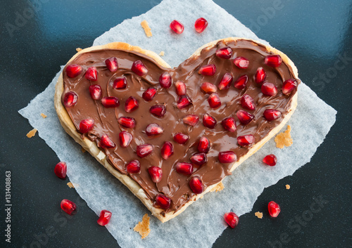 Fruit sweet heart shaped pizza with pomegranate seeds and nutella or chocolate cream on dark background - Valentines day party creative art dessert idea