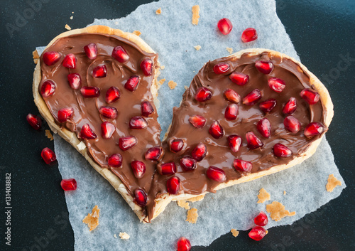 Broken heart concept - sweet heart shaped pizza with fruits - pomegranate seeds and nutella or chocolate cream on dark background - Valentines day party creative art dessert idea, top view