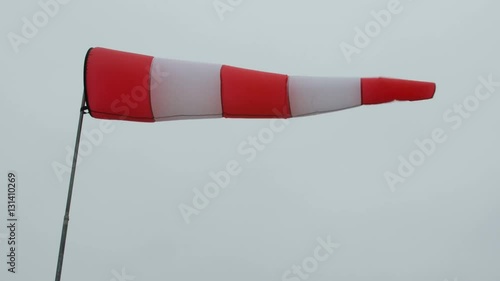 Inflated air sleeve windsock show direction of wind blowing near helicopter landing place site on background of gray sky.
